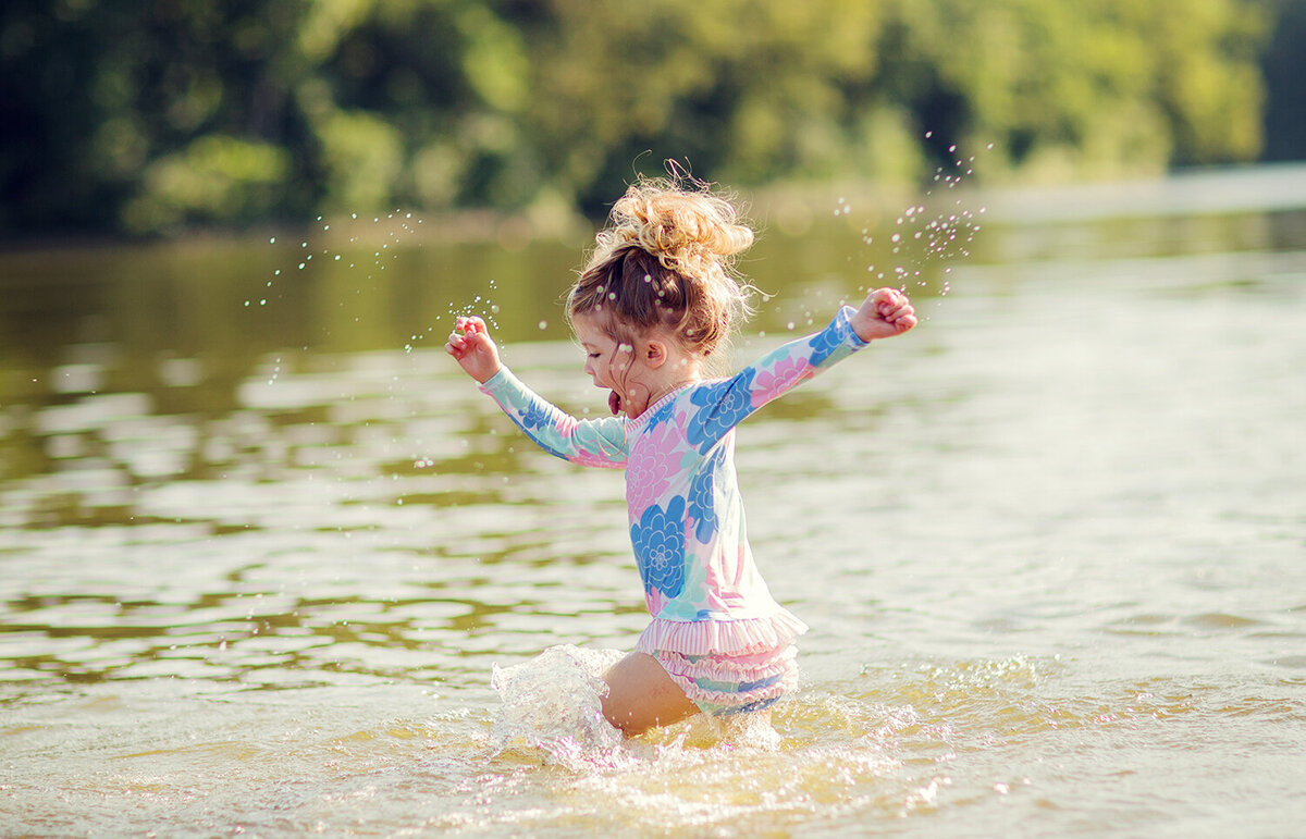 Toddler running though the lake gleefully, tongue out and arms wide.