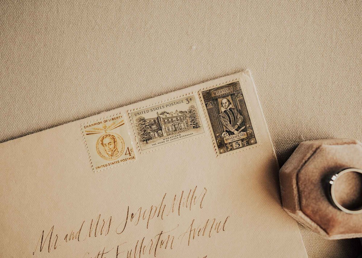 Maddie Rae Photography detail shot of an envelope that has three different antique stamps, the grooms ring is off to the side of the envelope