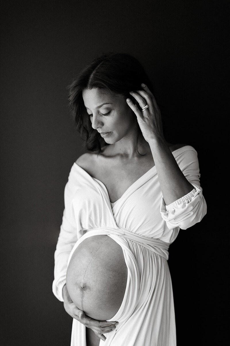 black mother wearing cream dress shows her growing bump in a black & white maternity photo