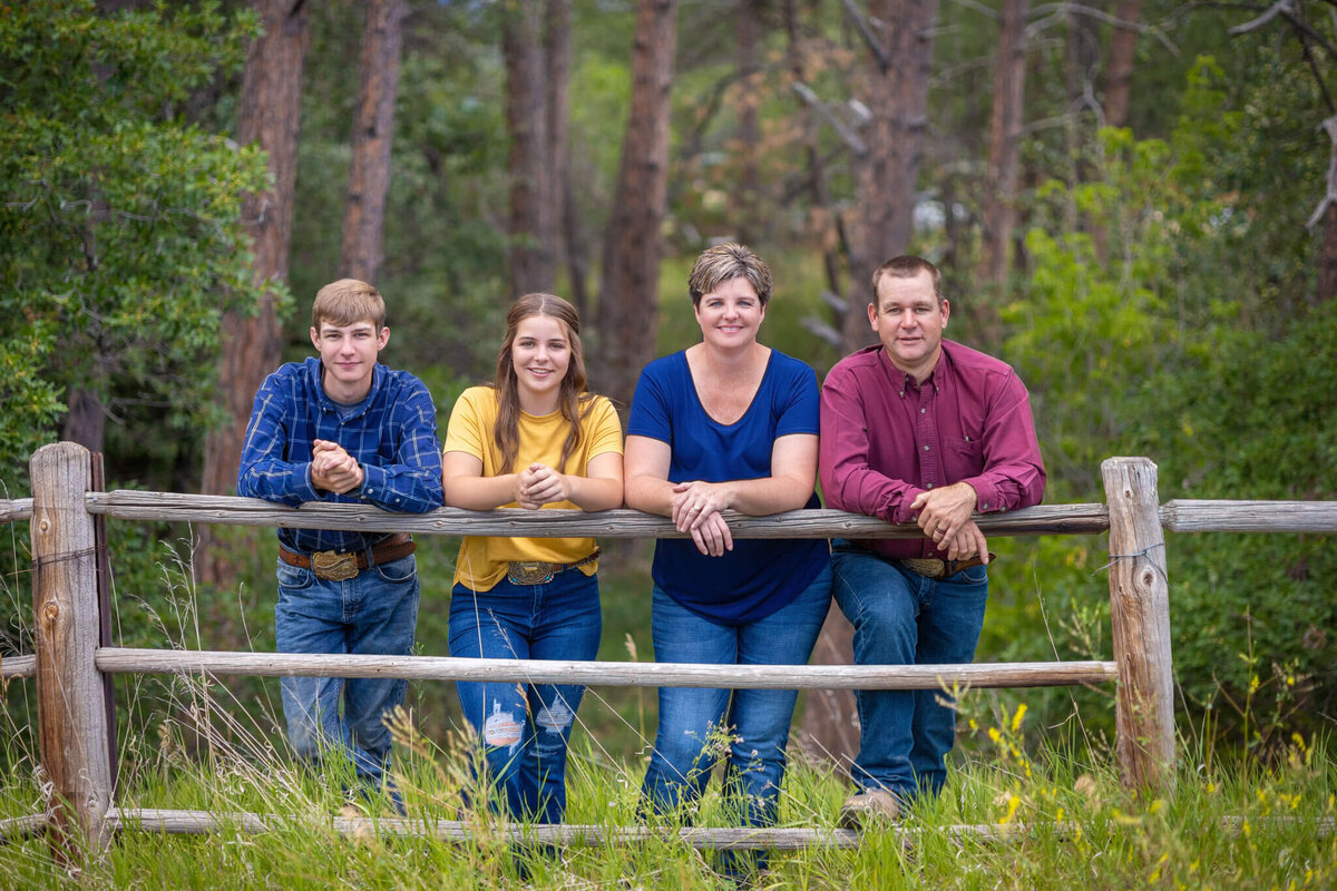 family of four leaning on a wodden fence smiling