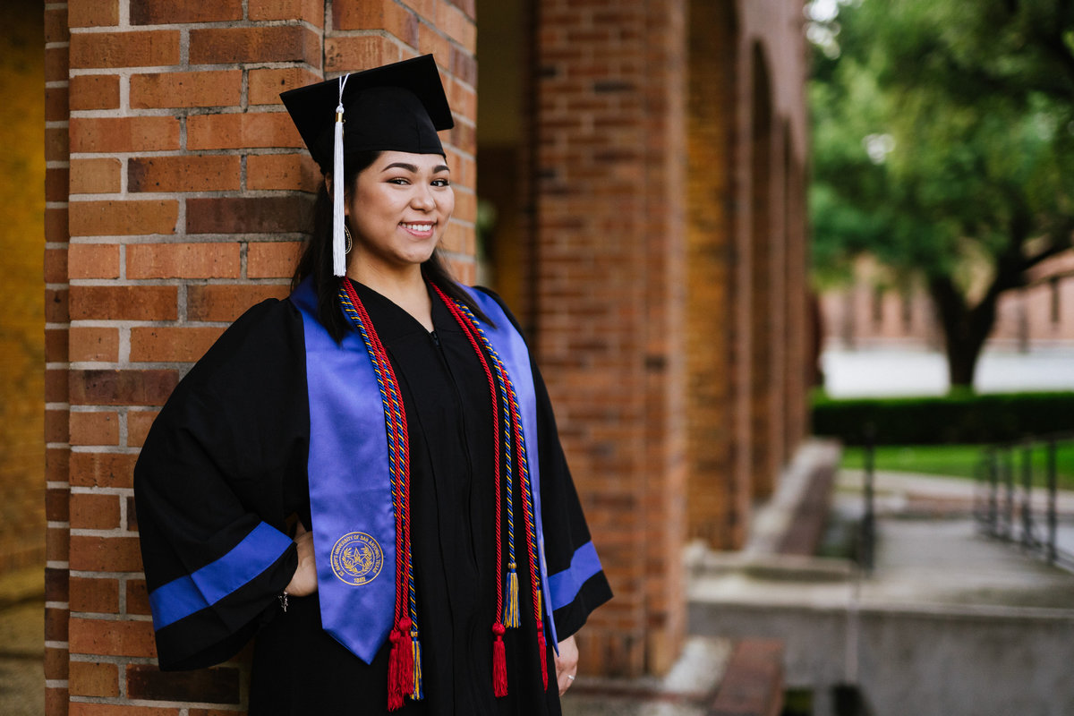 college senior leaning on a wall wearing cap gown