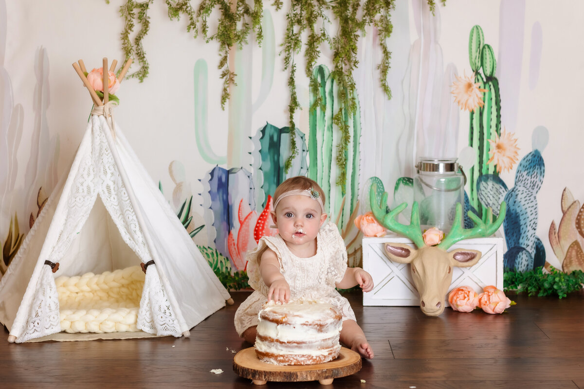 Cake Smash Photographer, a baby girl sits before cake a teepee and a cactus backdrop