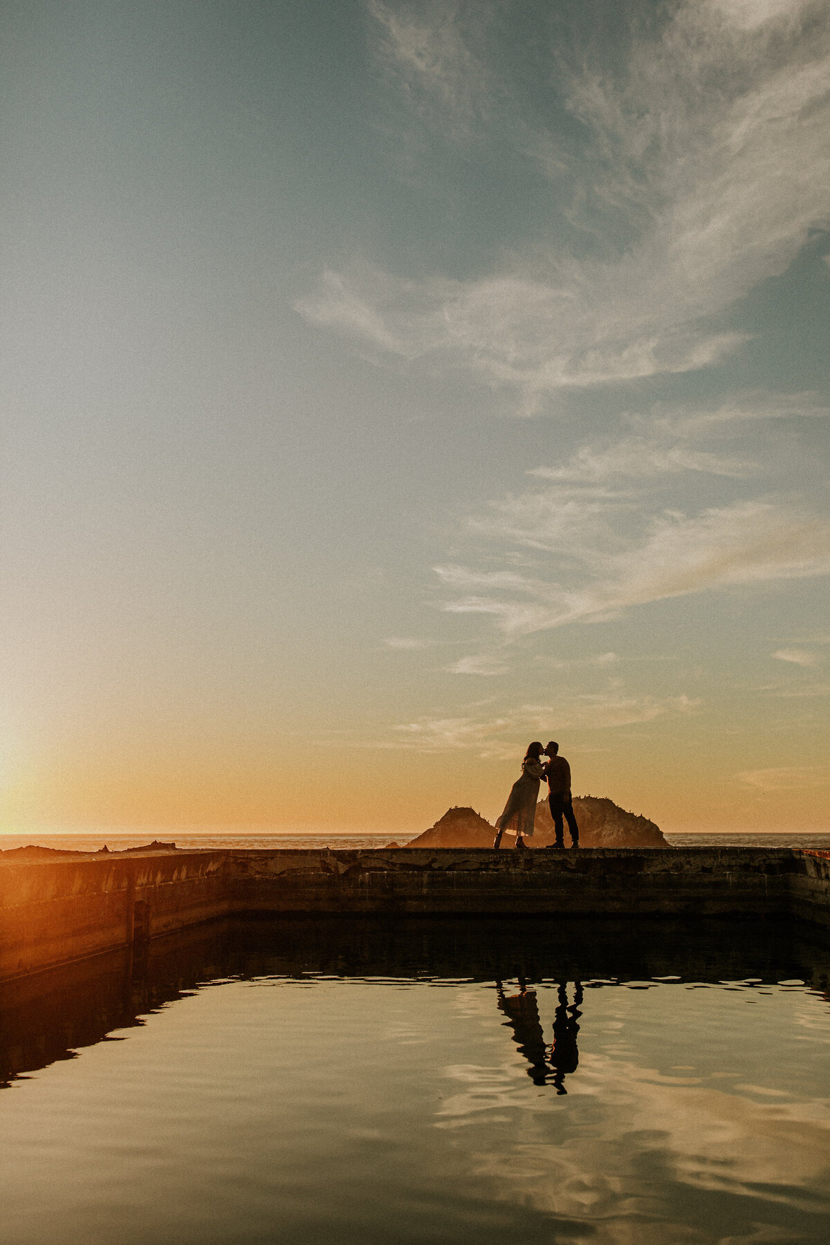 San Francisco maternity couple kiss at sutro baths with reflection on water and sunset sky