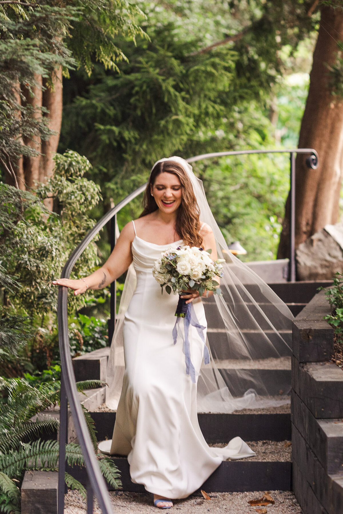 Bride-walks-down-steps-to-ceremony-in-wedding-dress-with-beautiful-white-flowers-at-winery-JM-Cellars-in-Woodinville-WA-near-Seattle-photo-by-Joanna-Monger-Photography
