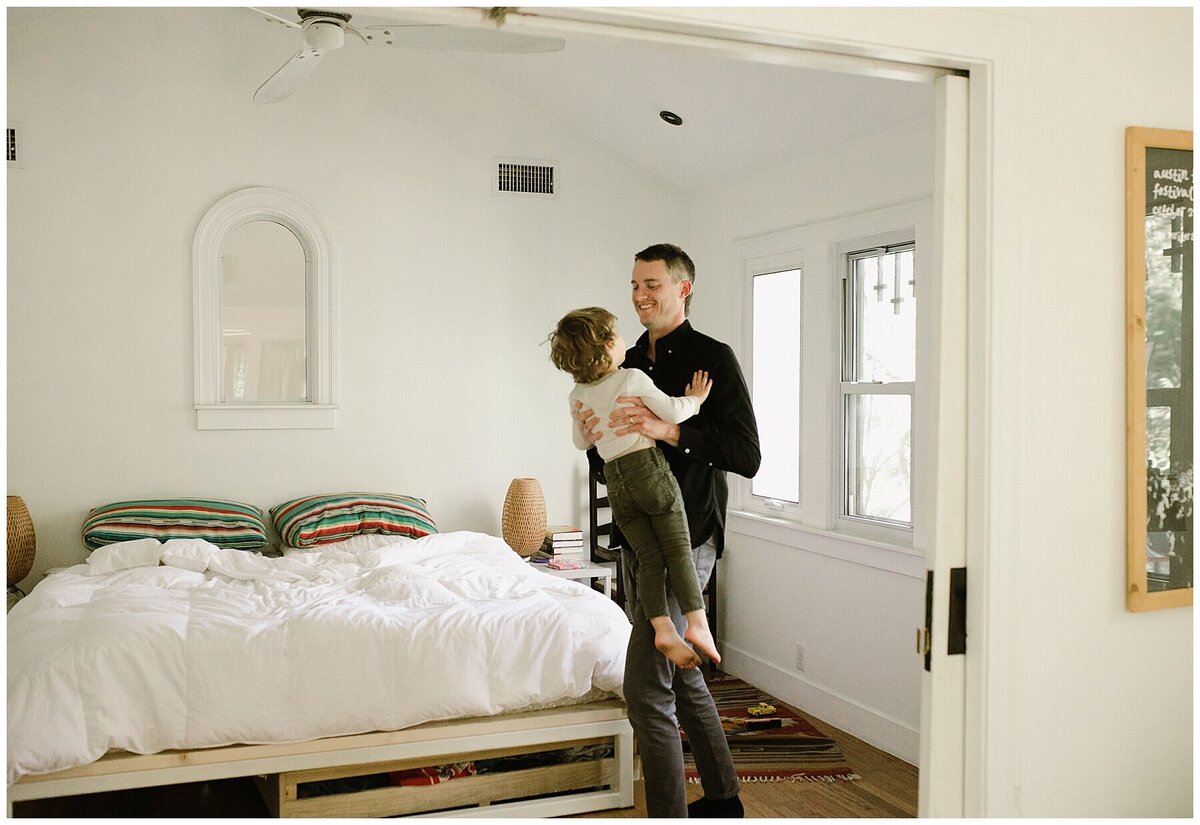 Father hold toddler son in his arms in the bedroom at sweet home family session in Austin by Amber Vickey Photography