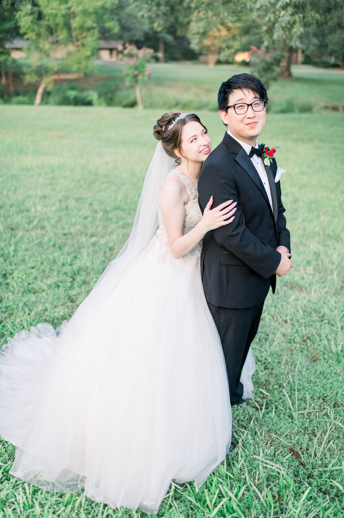 woman with crown and large white gown poses with her new husband in open field