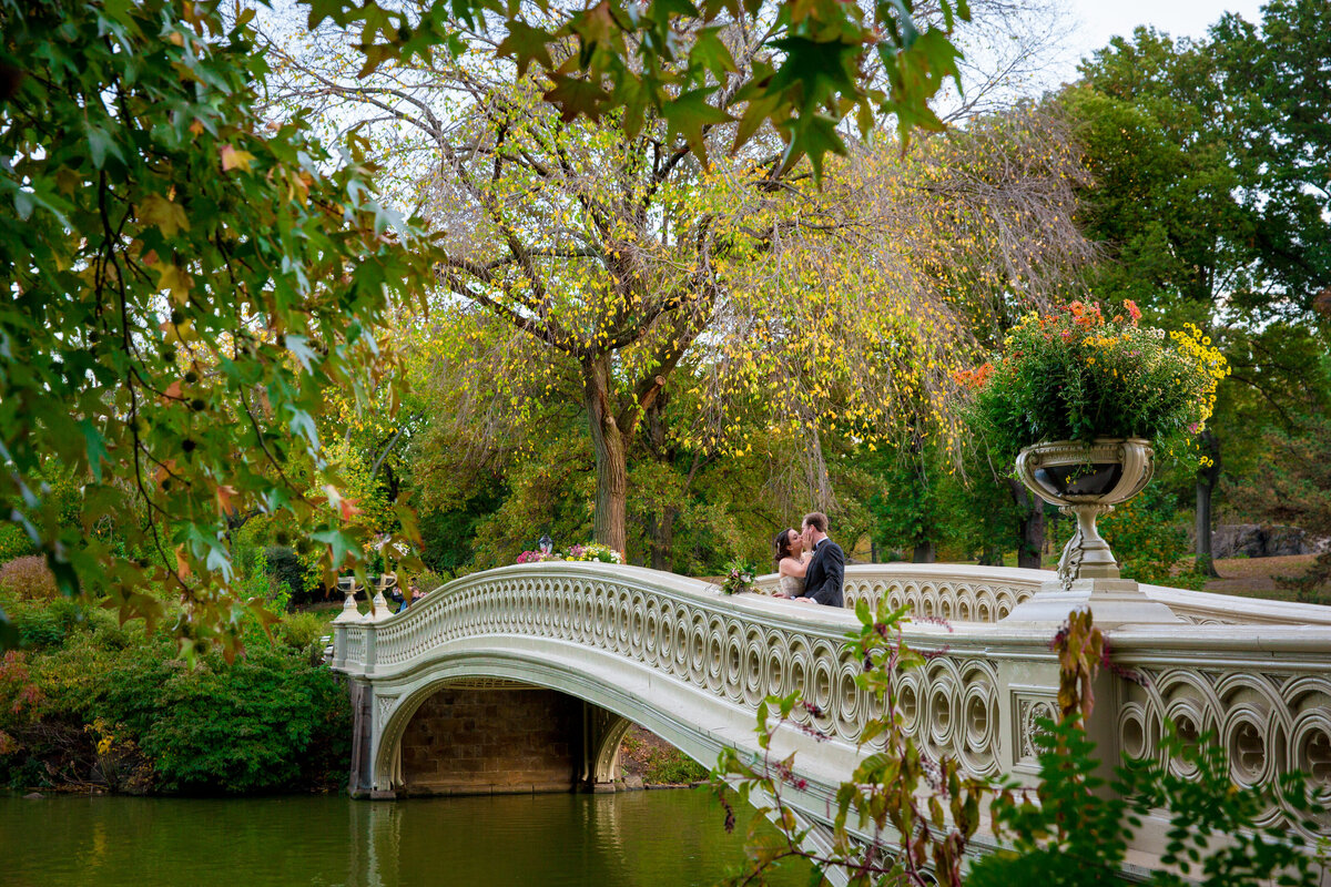 A wedding couple kissing on a bridge in a park.