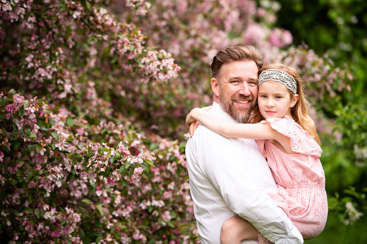 a father holds and hugs his daughter surrounded by blossoms during their family photography session in Ottawa