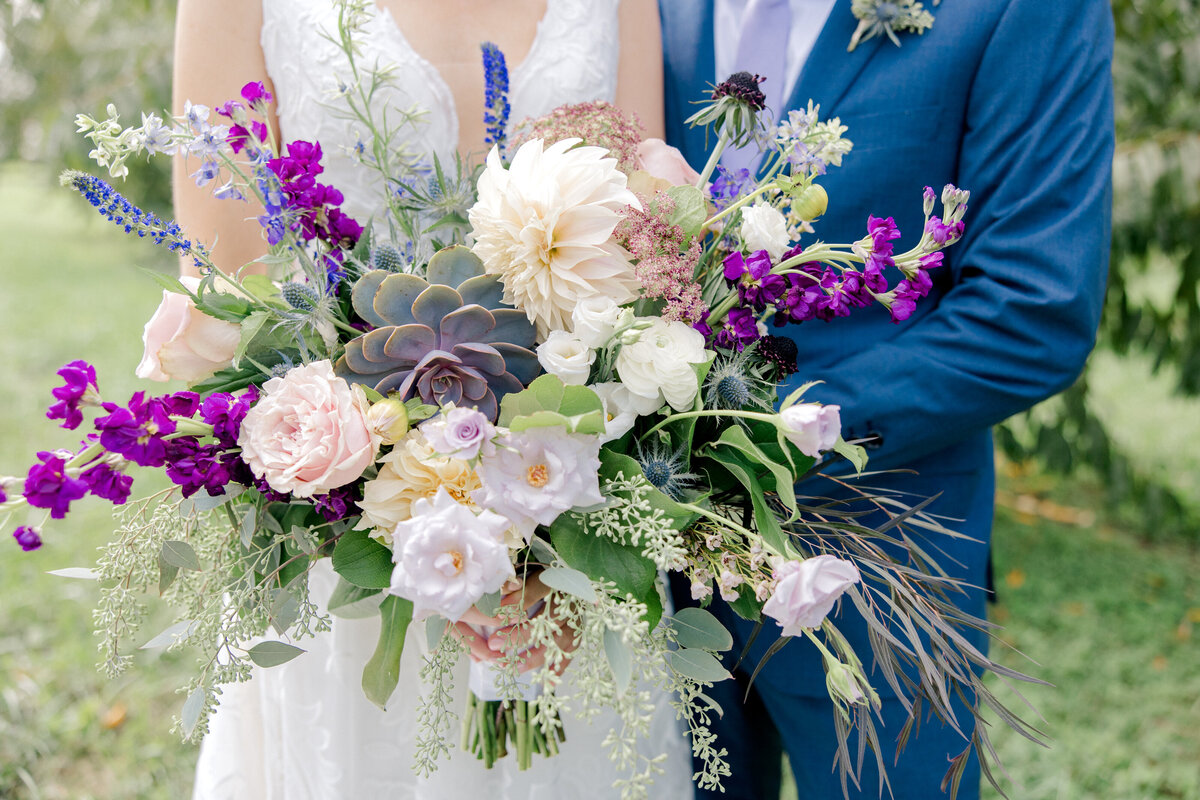 Bride and groom standing with purple and white flower bouquet