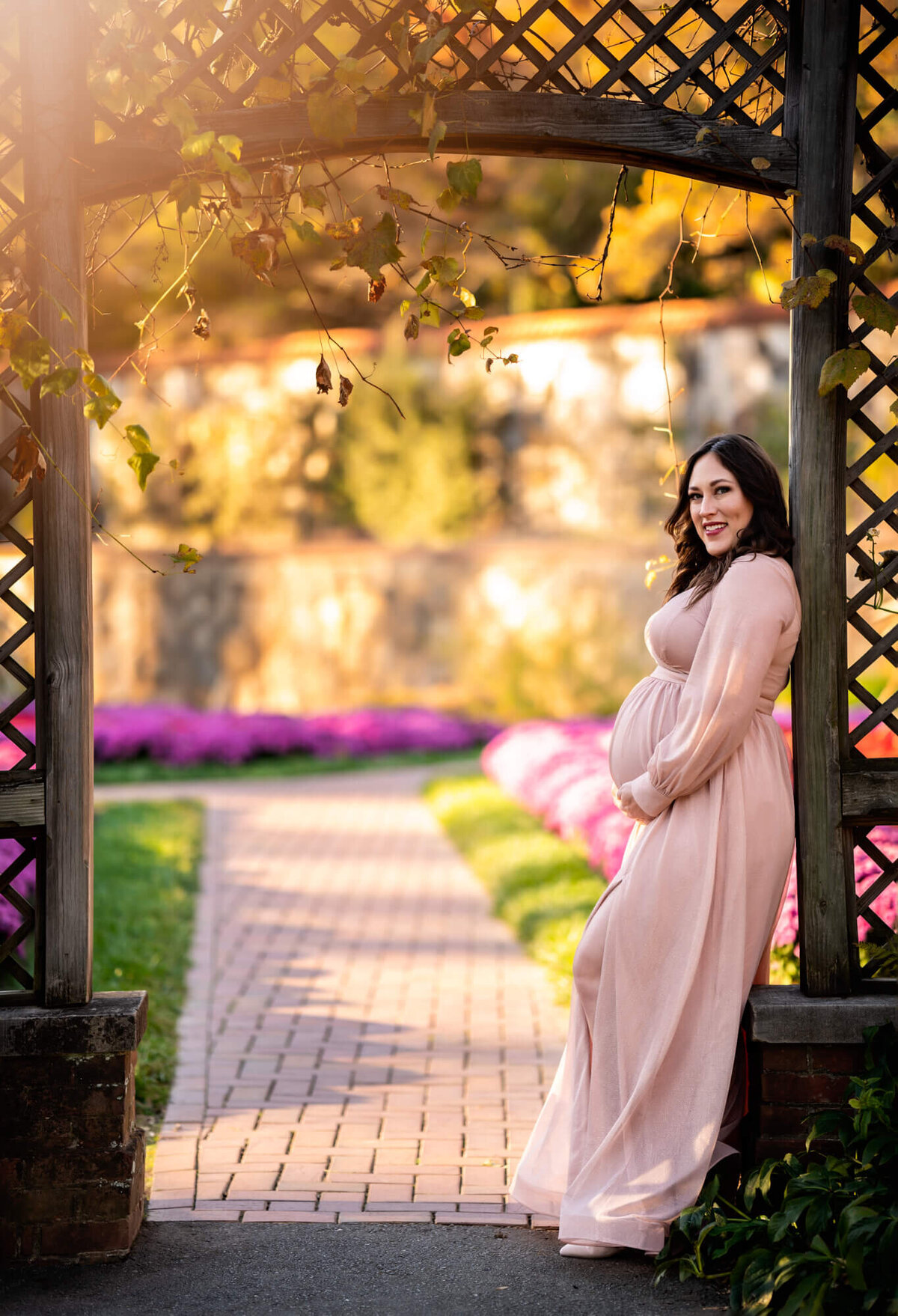 A mama to be in a long pick dress cradles her bump while standing at the gardens at the Biltmore Estate
