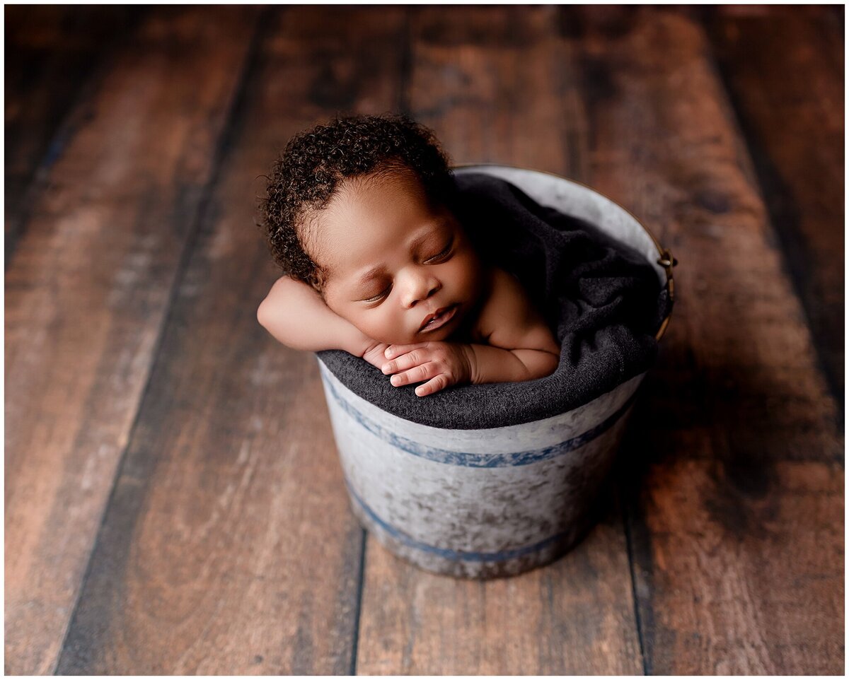 A newborn baby peacefully sleeping with head resting on hands in a bucket.