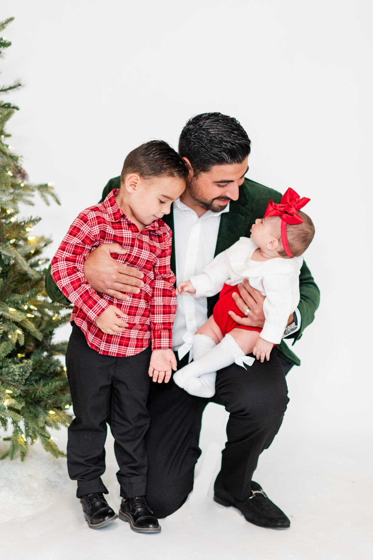 dad with daughter and son wearing Christmas outfits in front of a Christmas tree by Miami Christmas Mini Session Photographers