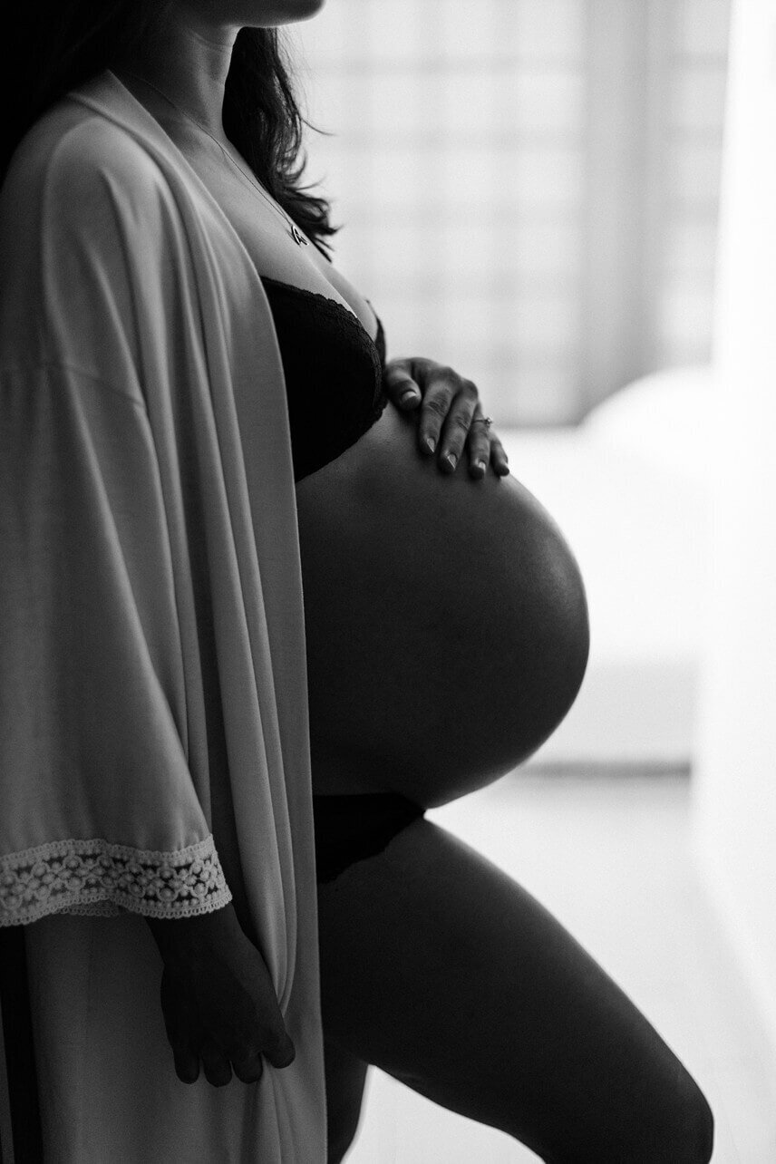 Black and white photo of a pregnant mom gently touching her baby bump.