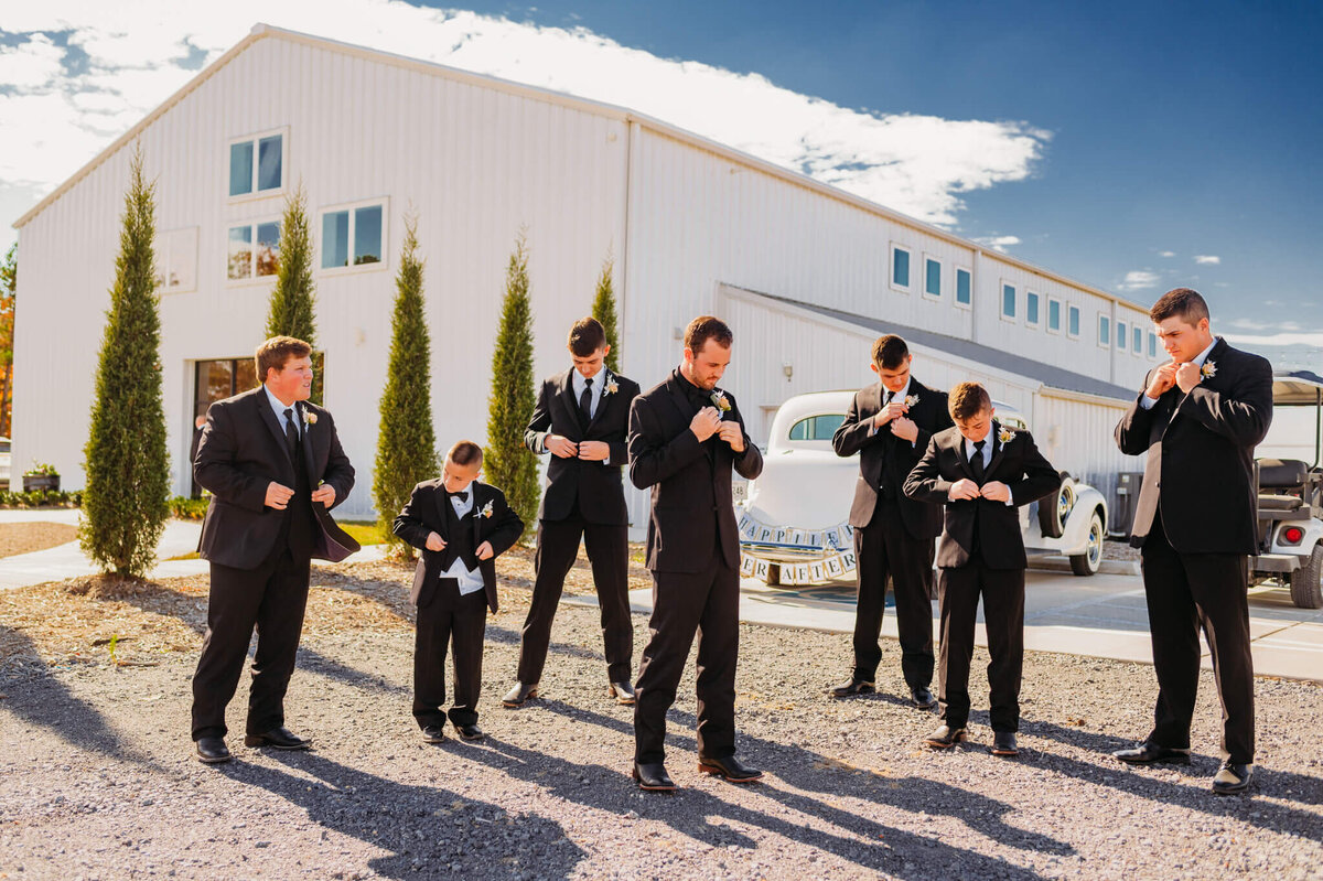 Photo of a groom and his groomsmen buttoning their jackets in front of a white venue