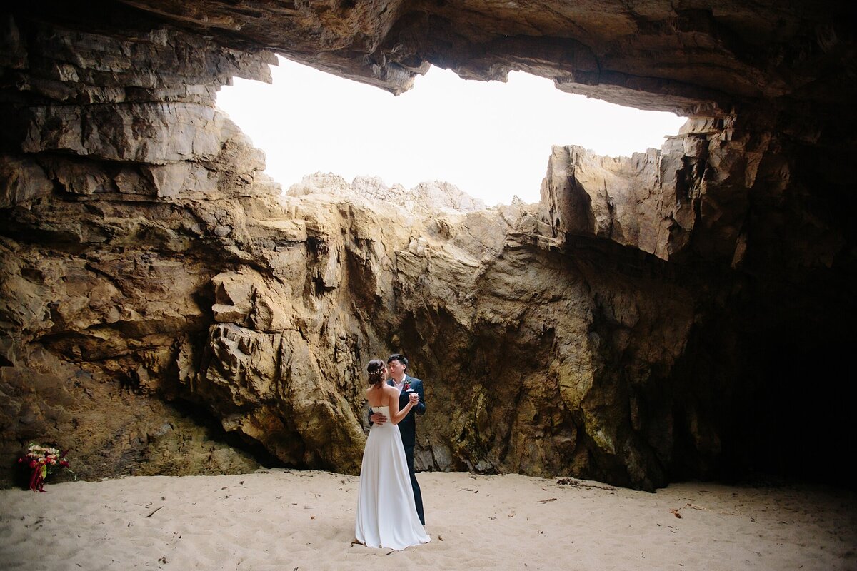 The bride and groom dance together in a cave on the beach in Big Sur.