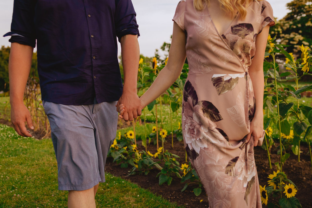 engaged couple holding hands walking through field of sunflowers