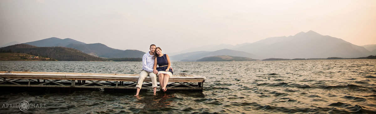 Cute couple sits on the dock at Lake Dillon at Sunset Engagement Session in Summit County Colorado