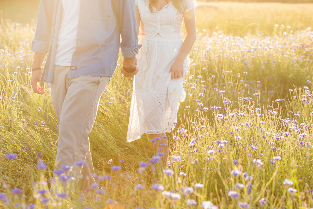 couple walking through wildflower field at sunset during golden hour glow