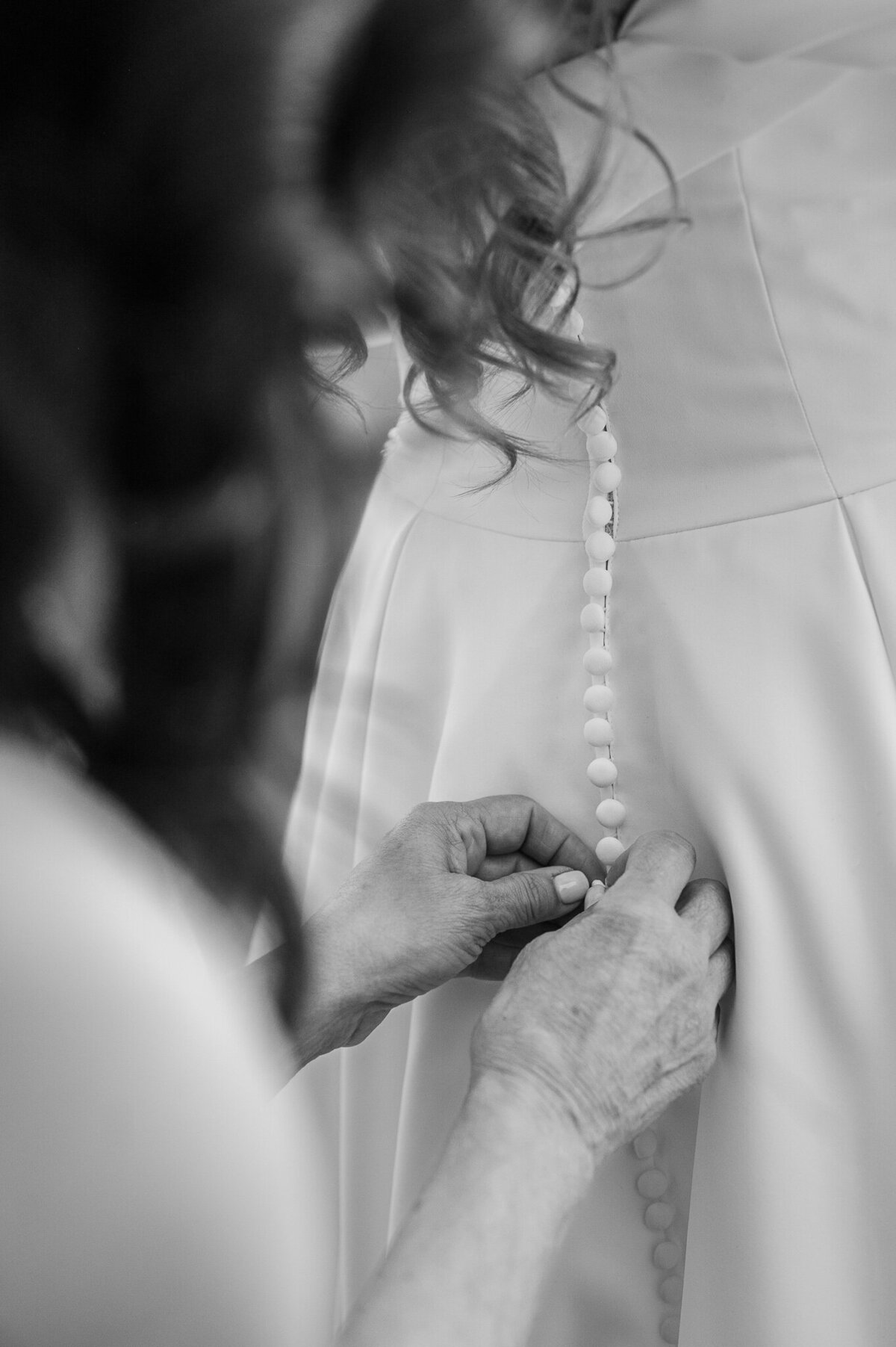 A mother of the bride zipping up her daughter's wedding dress by JoLynn Photography
