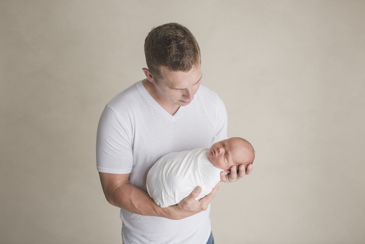 a father holding his baby boy with white clothes on