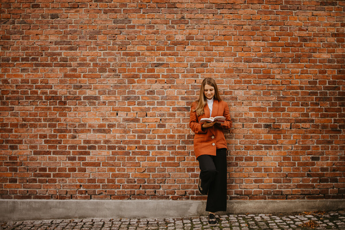 Barbora is reading a mindset book while she leans against a brick wall