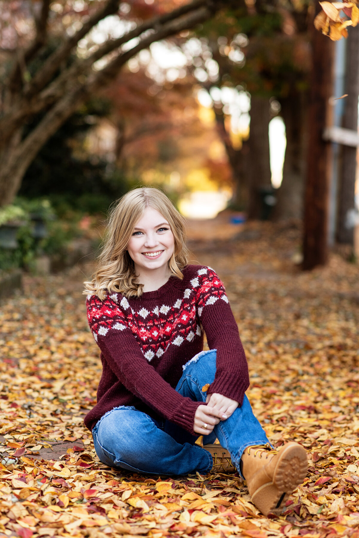 St Catherines high school senior wears a fall sweater and poses among leaves on sidewalk.