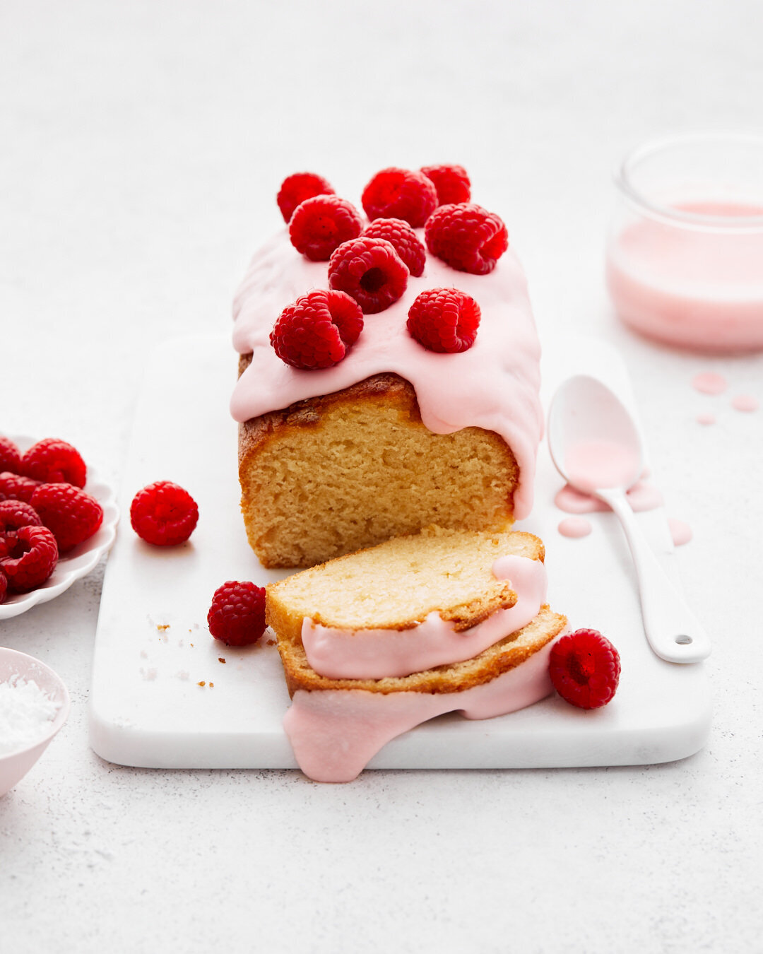 A loaf cake with raspberry sauce and raspberries on top.