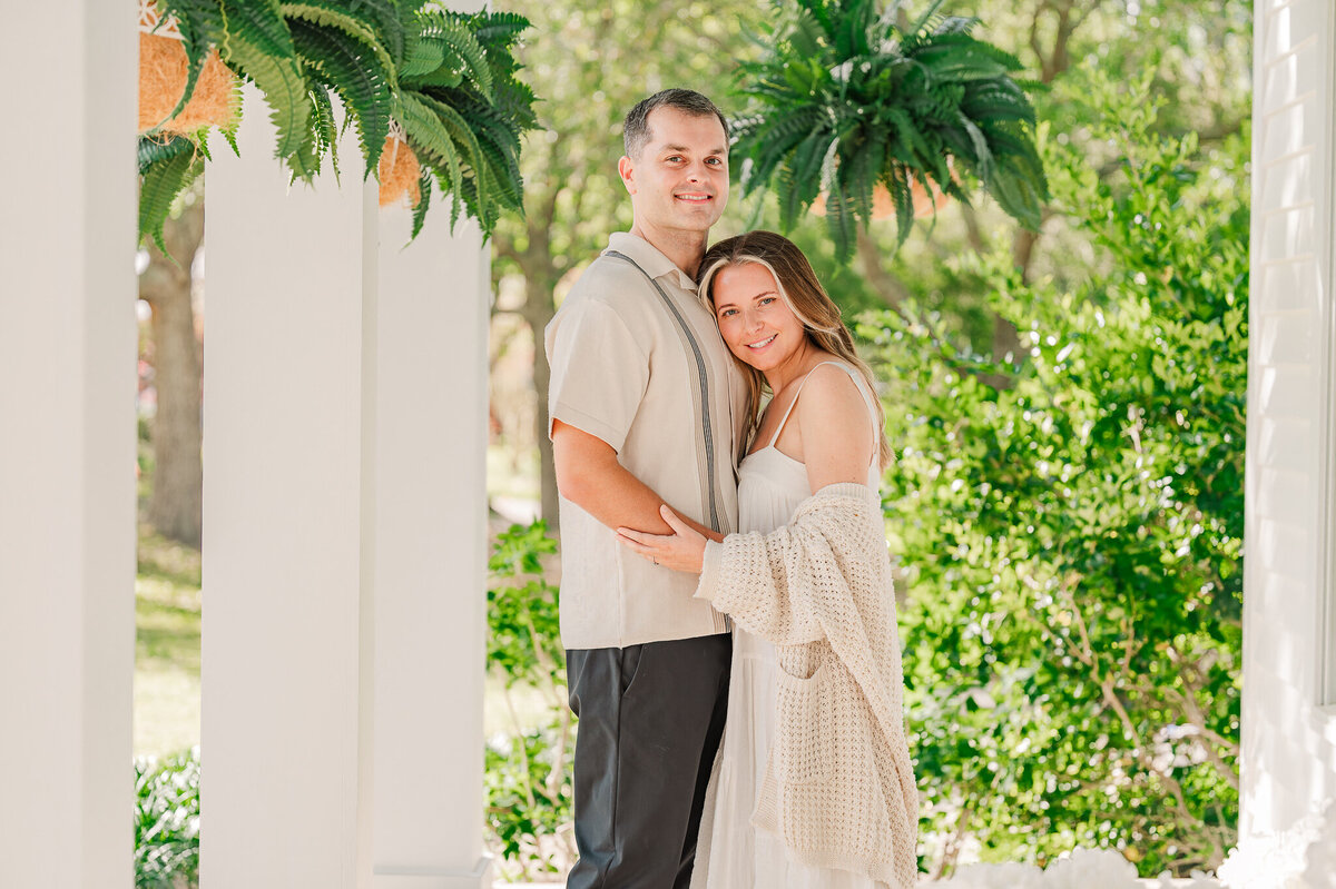 An engaged couple embracing on the porch of a historic estate home in Wilmington during the spring enjoying their Wilmington wedding photos