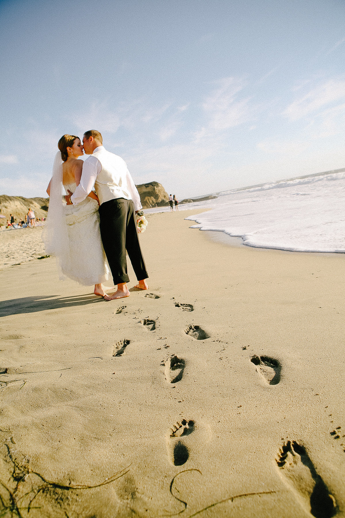 A bride and groom walk along the beach at their wedding at the Ritz-Carlton in Half Moon Bay.