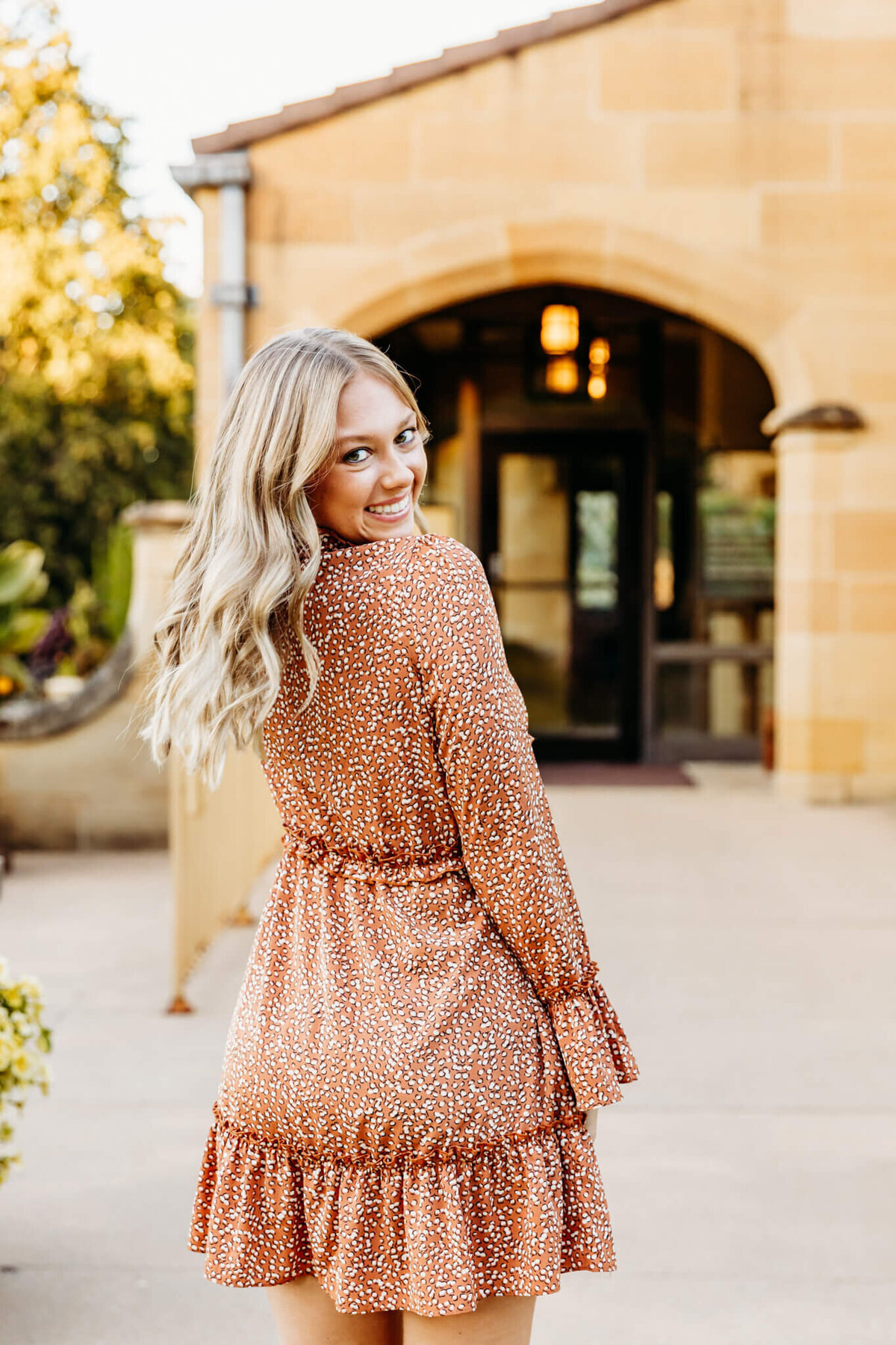 blonde high school girl spinning in her orange dress and looking back as she smiles for her senior photos