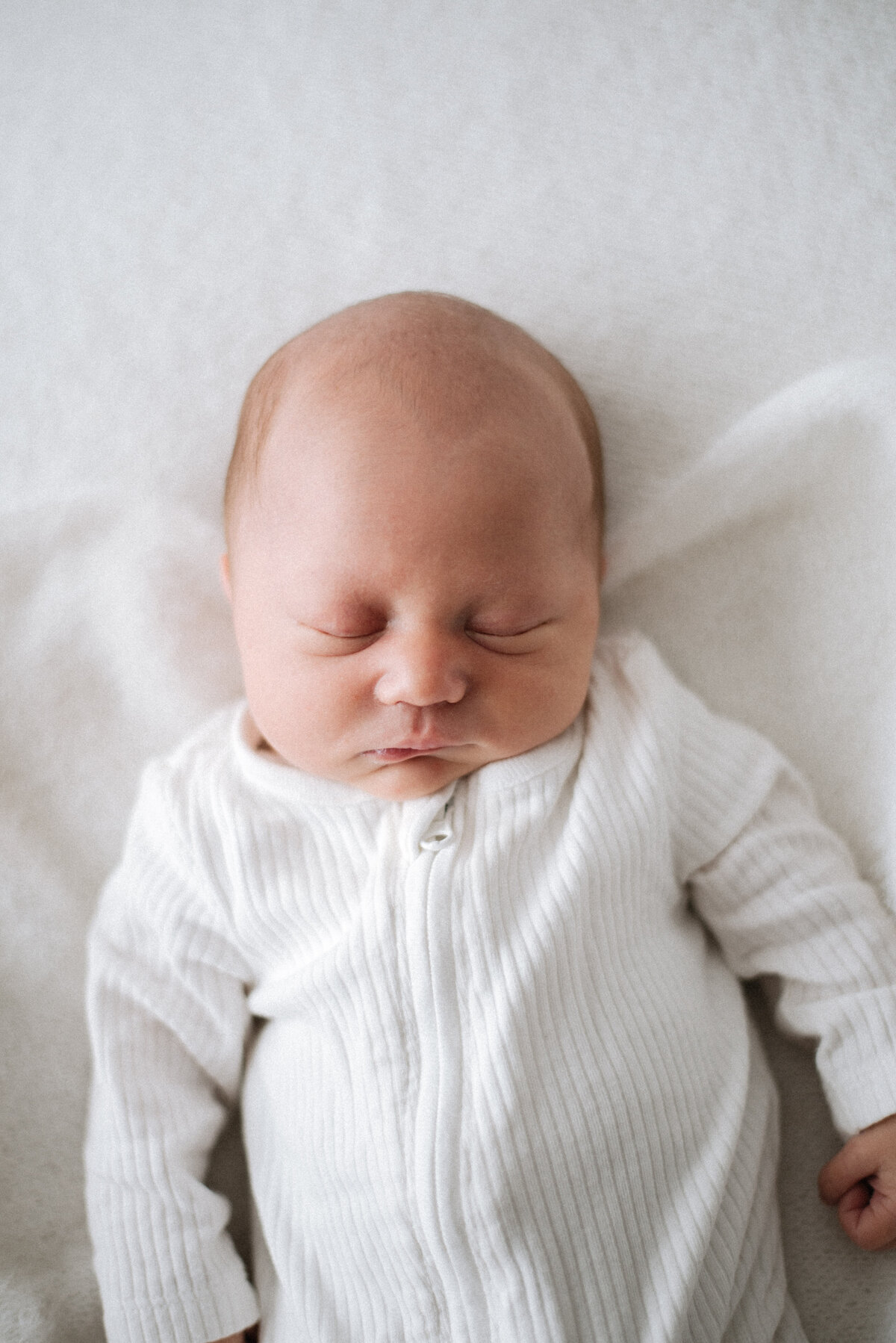 Baby boy sleeping in a white baby grow on a white blanket at billngshurst newborn photoshoot