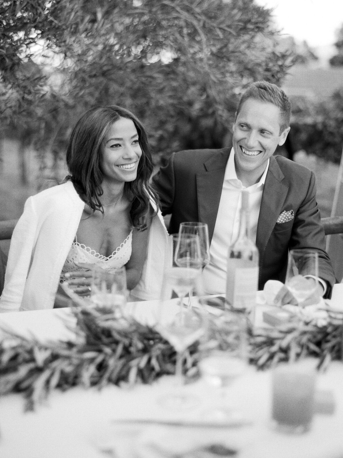 black and white image of couple laughing during toasts at welcome dinner