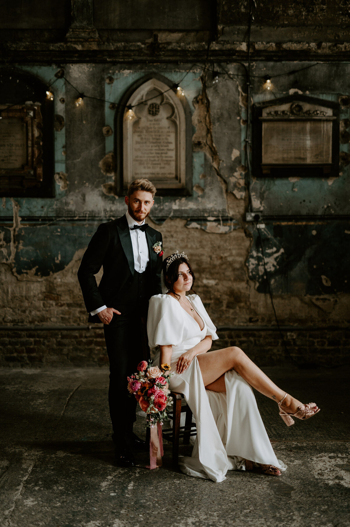 A groom stands over his bride who is sat on a chair after their wedding at The Asylum Chapel in London.