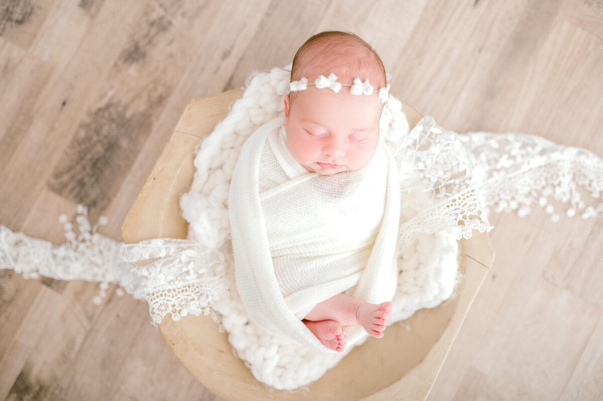 Baby sleeping in bowl on natural flooring, accented with white lace
