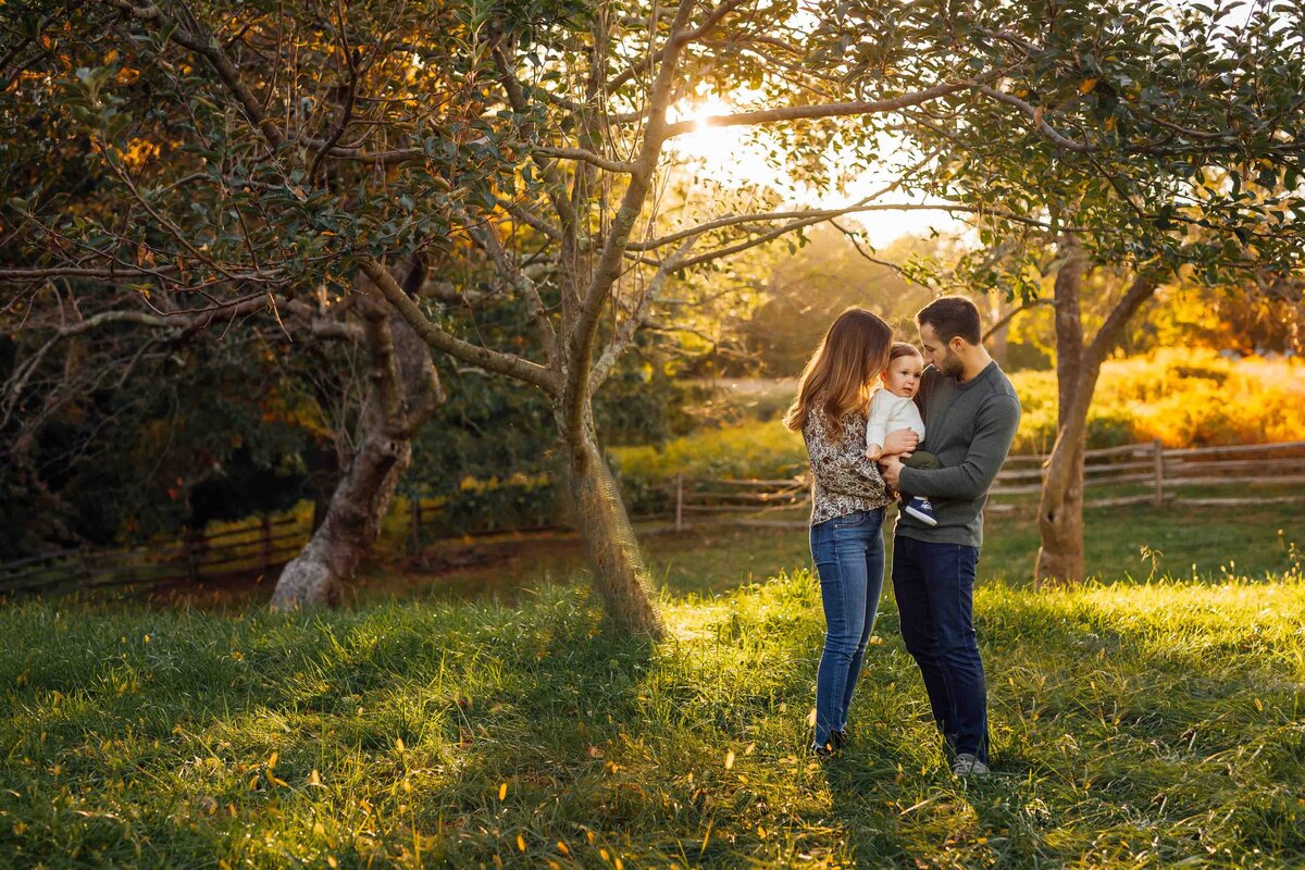 parents kissing baby in field