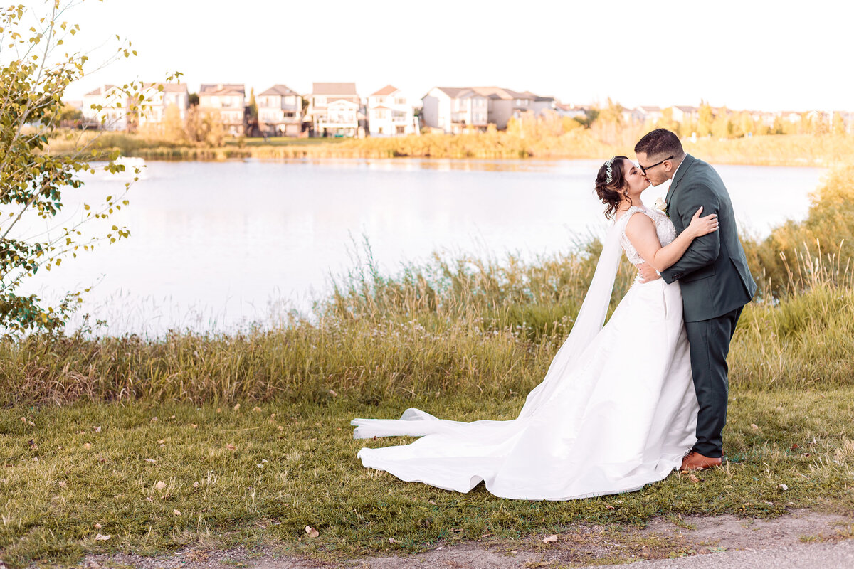 bride and groom kiss in front of a lake