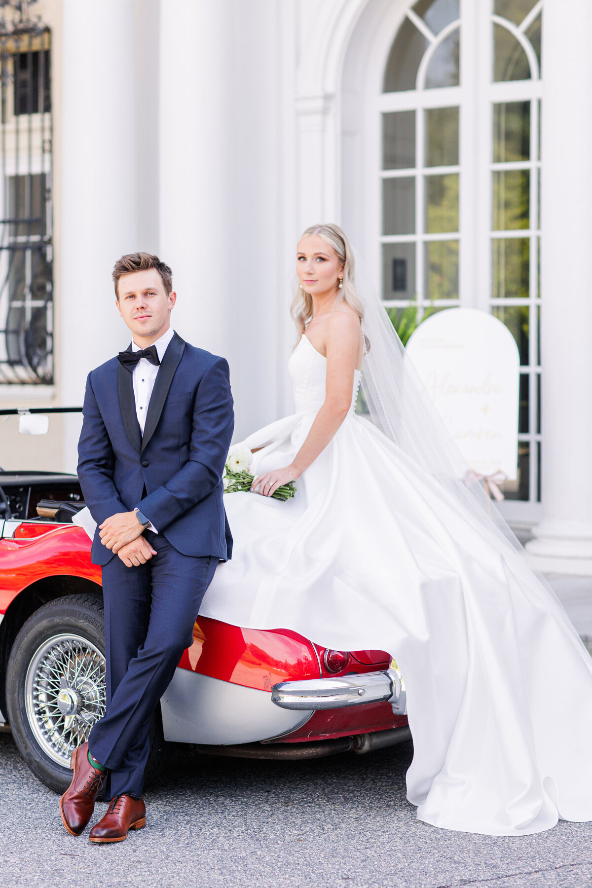 Groom leaning against a vintage car while bride sits on the car