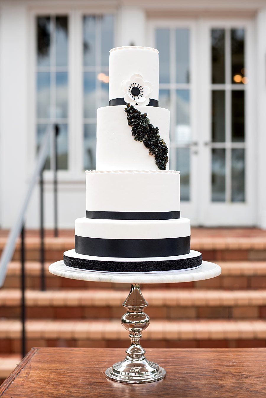 5 Tier White Fondant cake with black trimming, black rock candy cascading down it and an anemone flower
