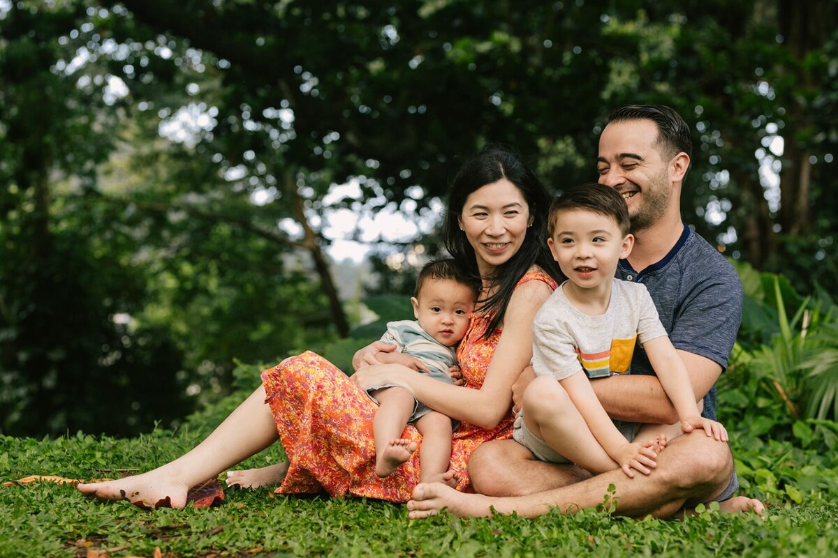 family of four sitting on the grass in a hawaii park