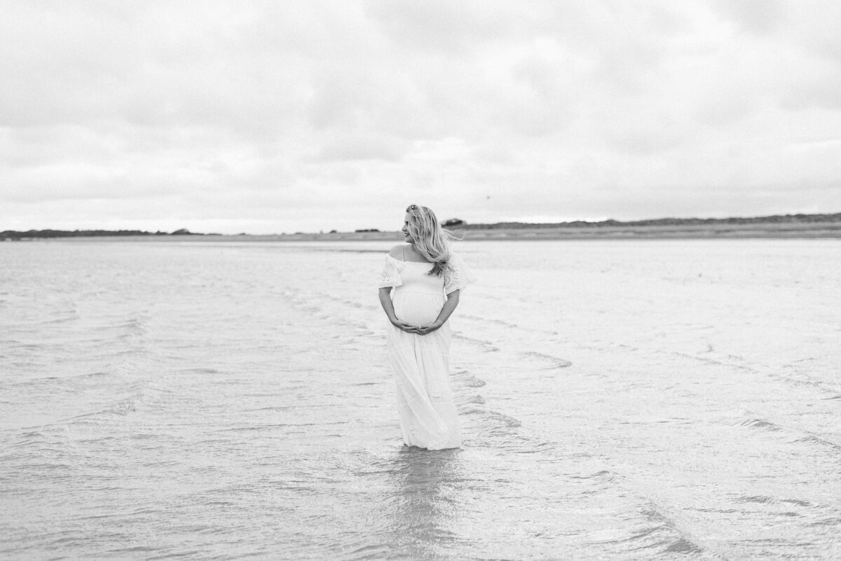 A pregnant women standing in the sea in white dress at a Billingshurst  maternity photoshoot