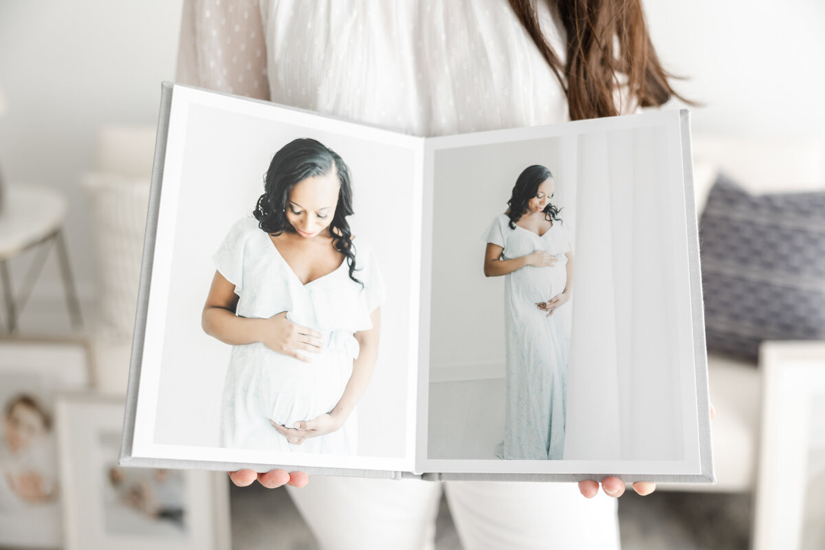 Woman holds heirloom photo album open to a spread of maternity portraits
