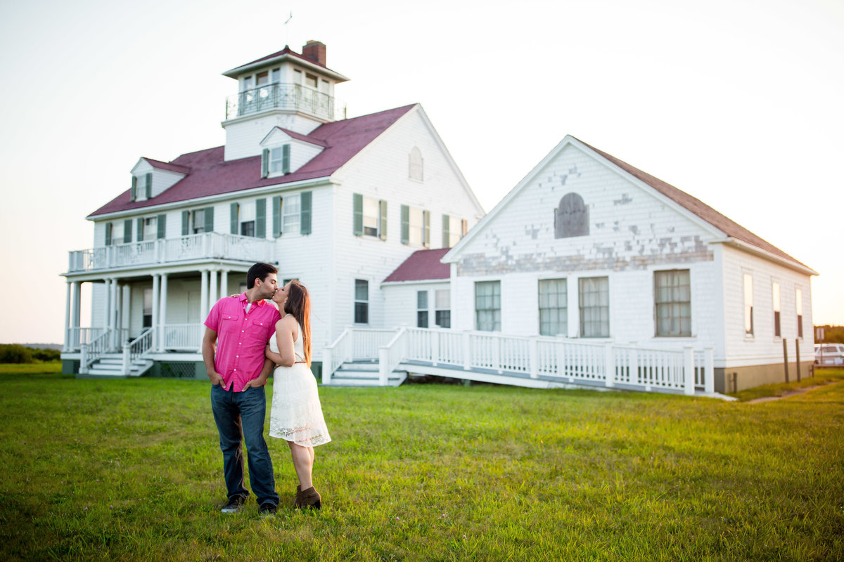 A couple kisses in front of a farmhouse.