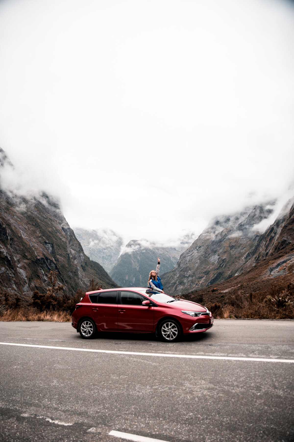 Red car traveling near Milford Sound, New Zealand