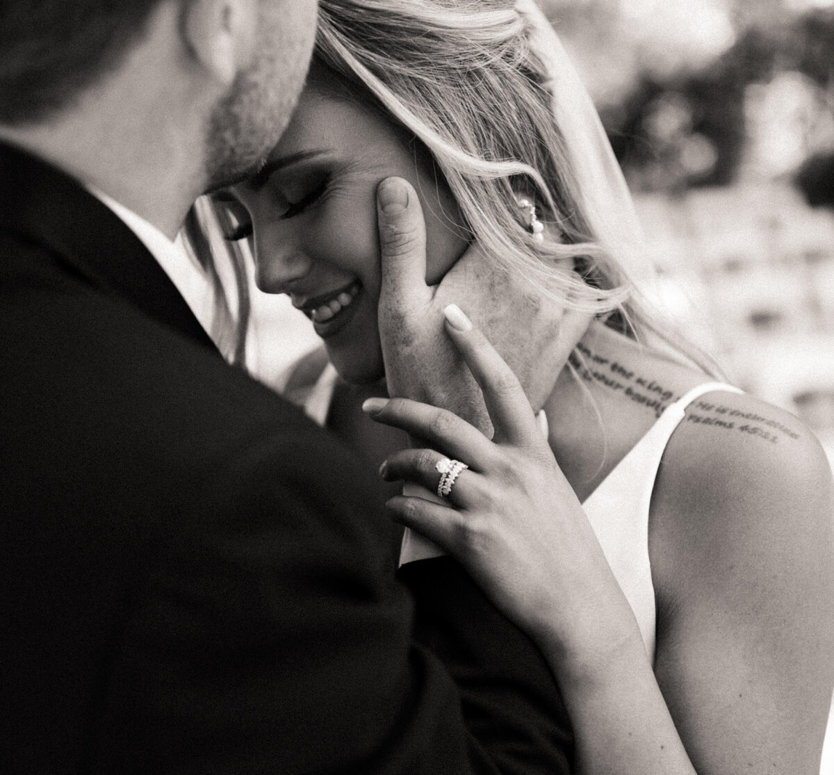 Close up of groom kissing bride's forehead as she smiles and looks down while holding his hand