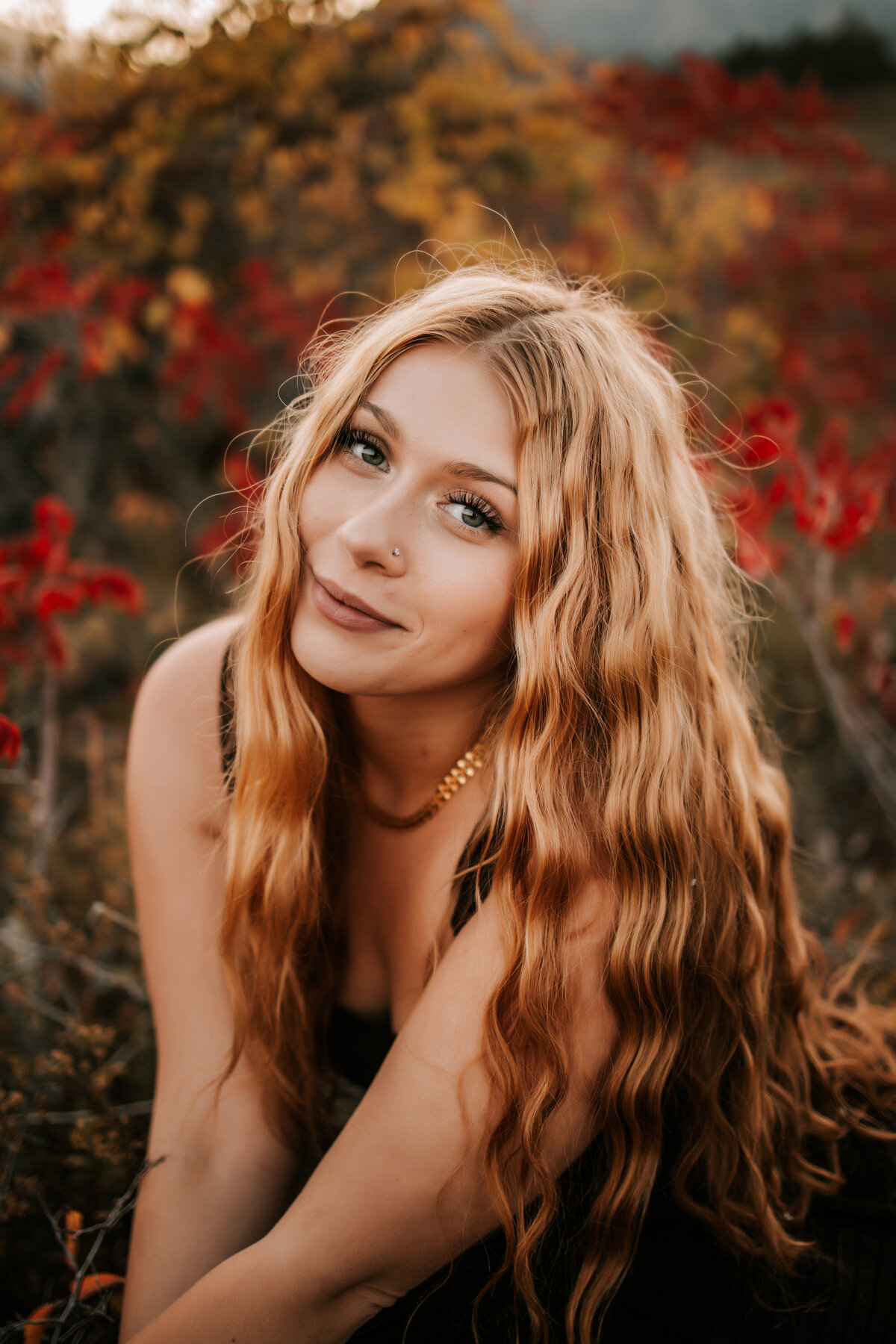 high school senior photo of girl with long wavy hair and fall foliage in the background