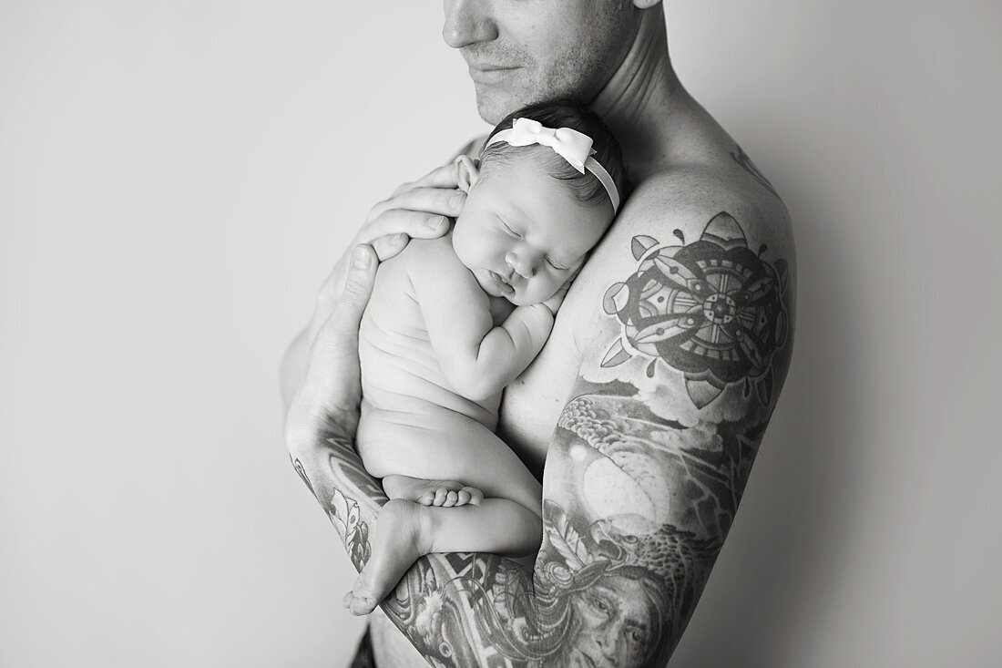 A tattoo covered father cradles his sleeping newborn daughter against his chest