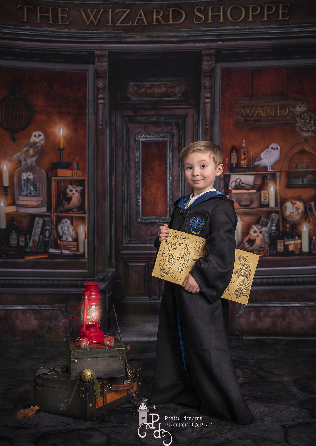 A young boy photographed in a wonderful Harry potter themed set up. He wears a blue robe and stands next to a lantern and pile of vintage suitcases. Photographed in Sonia Gourlie Fine Art Photography's studio in Ottawa.