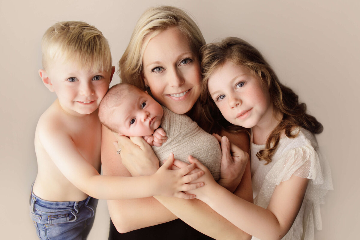 mom with 3 young children including newborn hugging