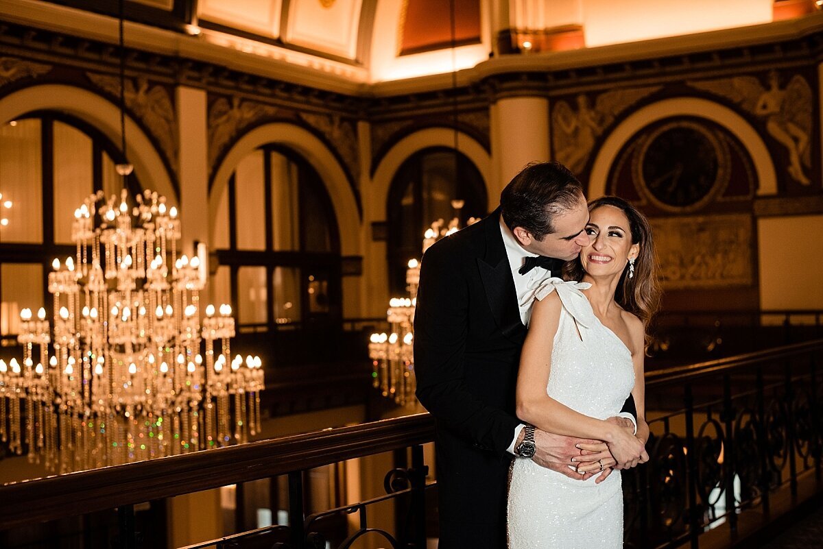 Groom kissing his wife on the cheek on the top floor of Union station in Nashville with the chandeliers behind them