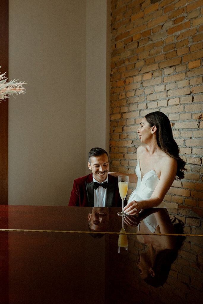 Bride and groom at piano in The Garret, historical and sophisticated, Calgary, Alberta wedding venue, featured on the Brontë Bride Vendor Guide.